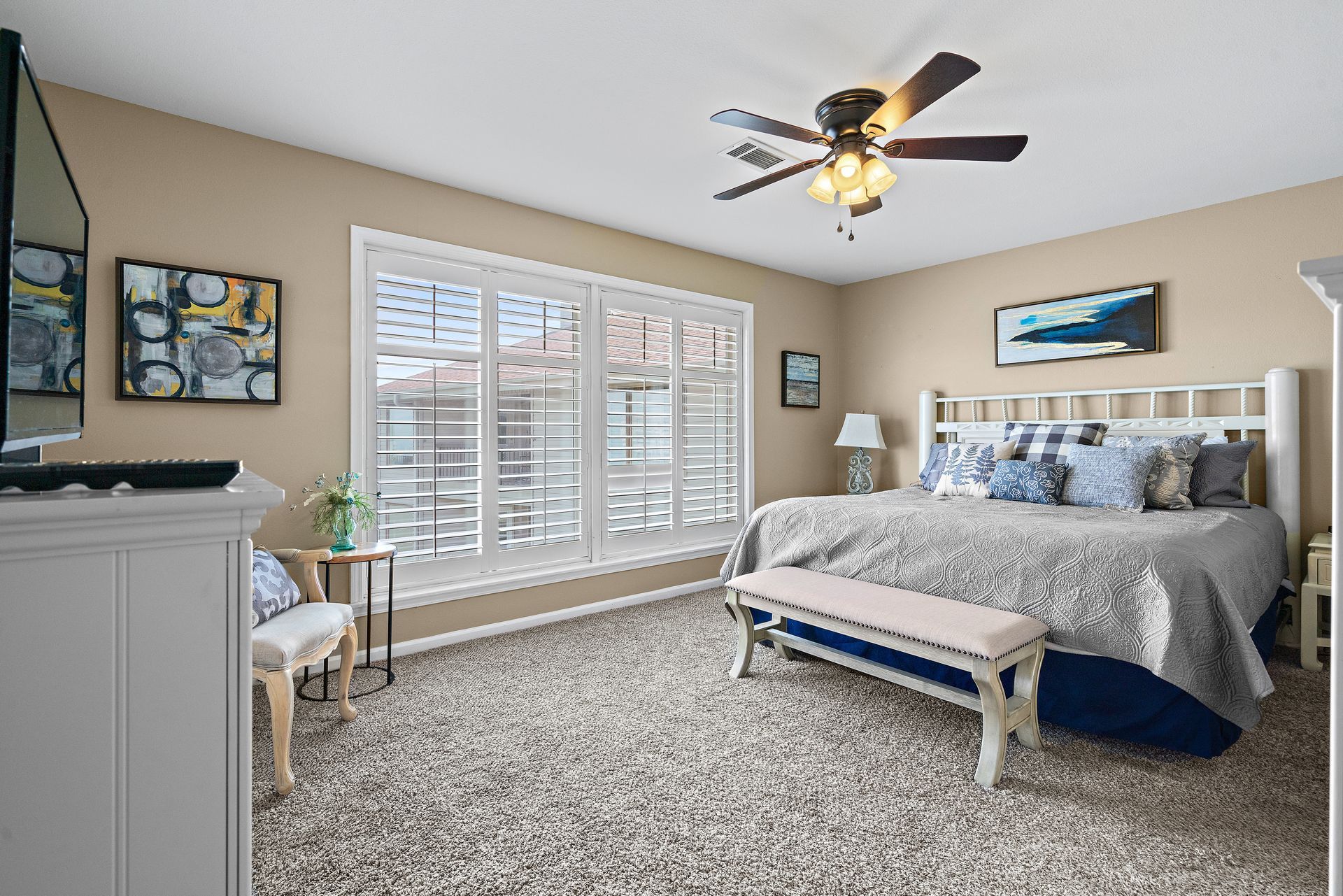 A bedroom with two beds , a bench , and a ceiling fan.
