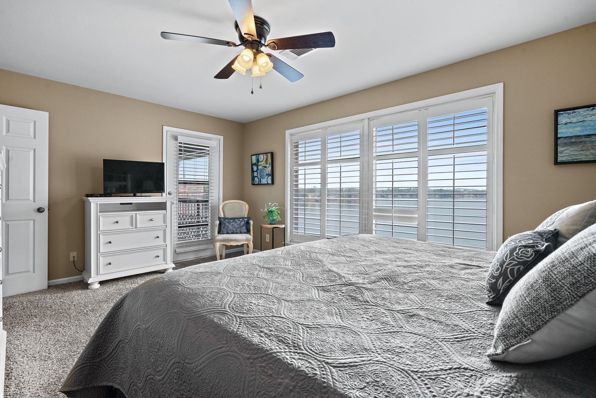 A bedroom with a king size bed , a ceiling fan , a television , a dresser and a chair.