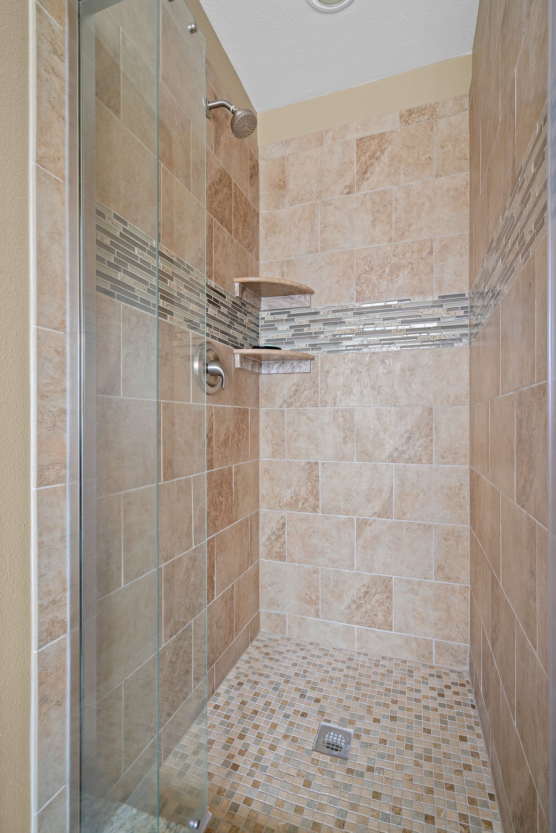 A walk in shower with a glass door and tiled walls.