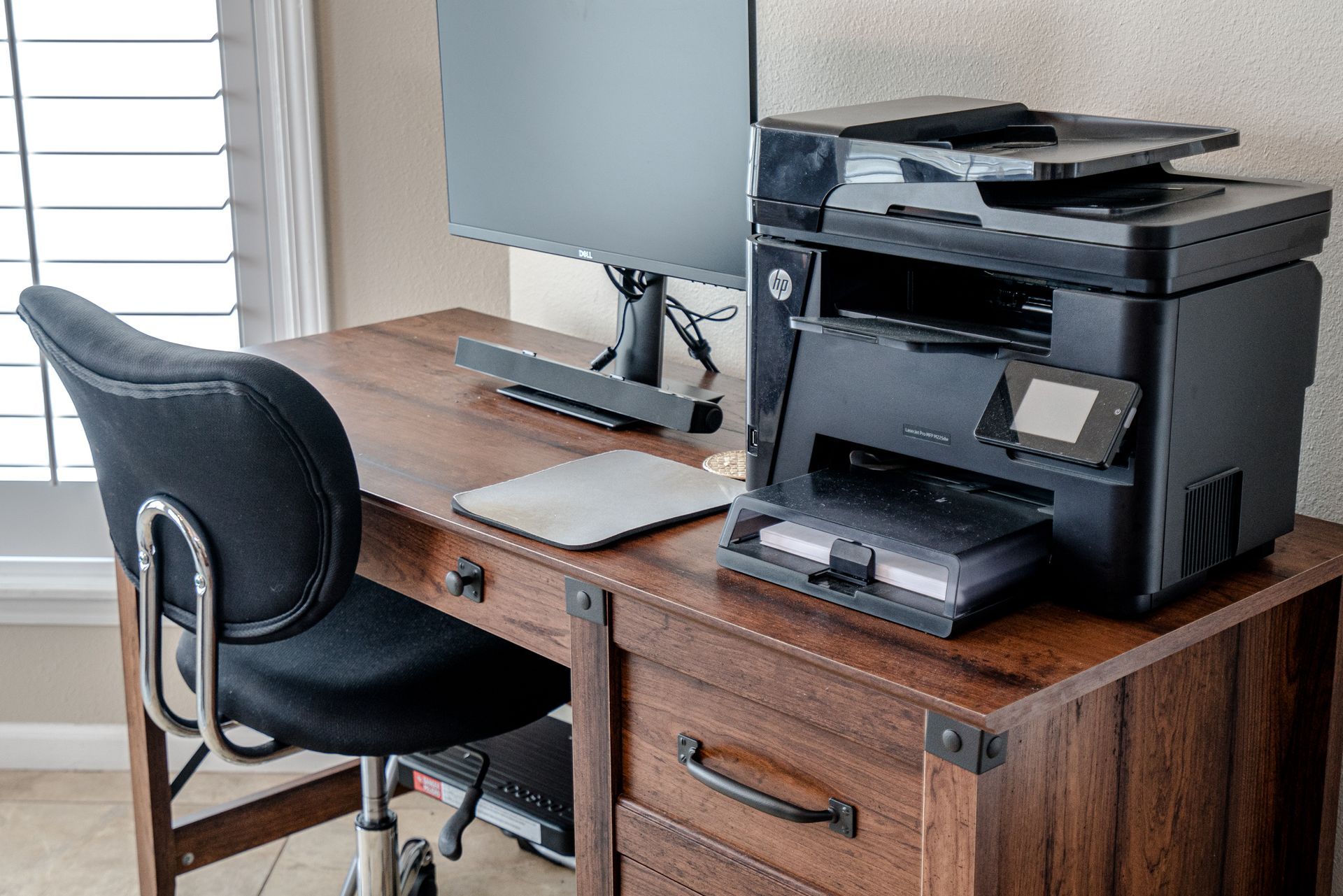 A printer is sitting on top of a wooden desk next to a computer.