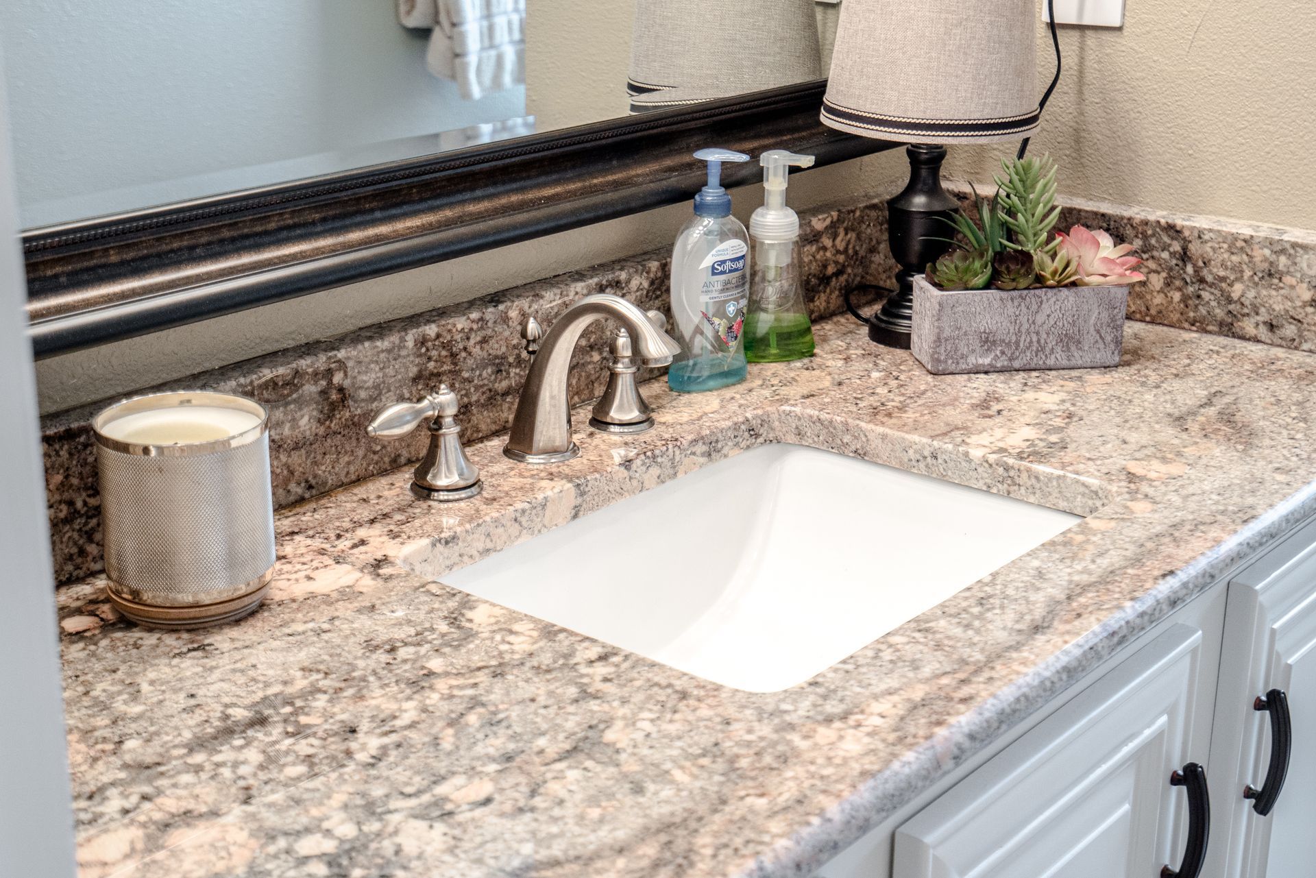 A bathroom sink with a granite counter top and a mirror.