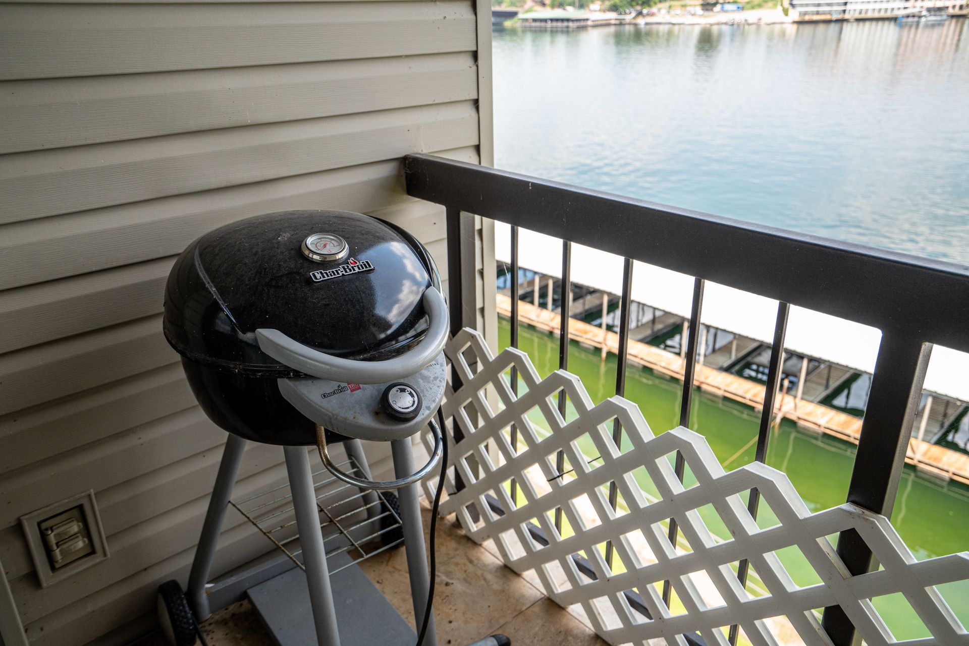 A grill is sitting on a balcony overlooking a body of water.
