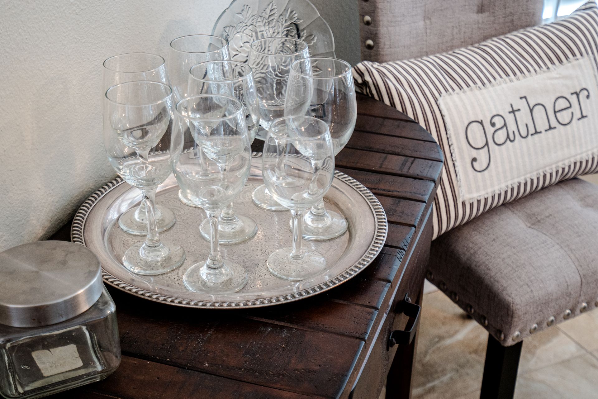 A tray of wine glasses sits on a table next to a pillow that says gather