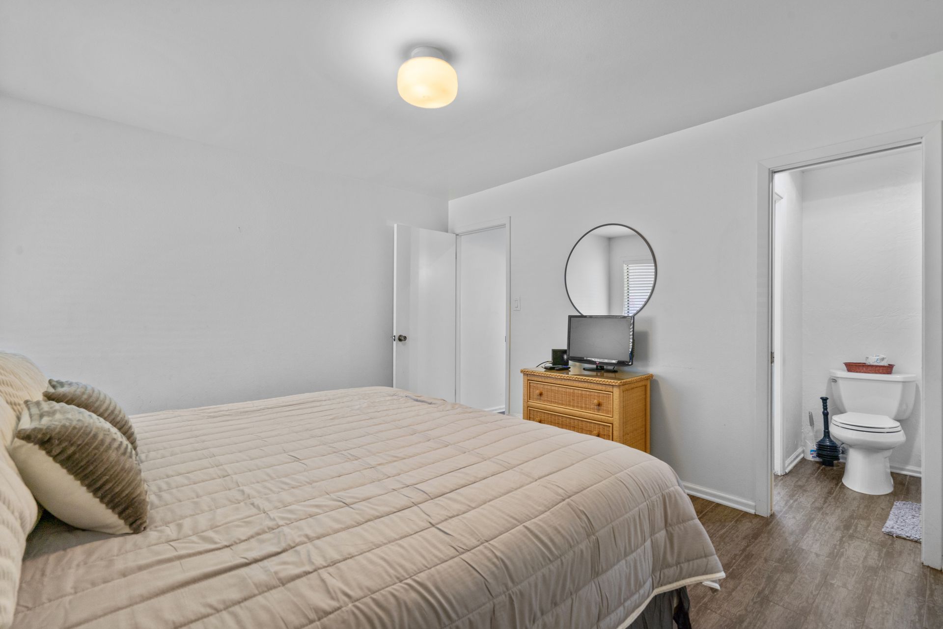 A bedroom with a bed , dresser , mirror and toilet.