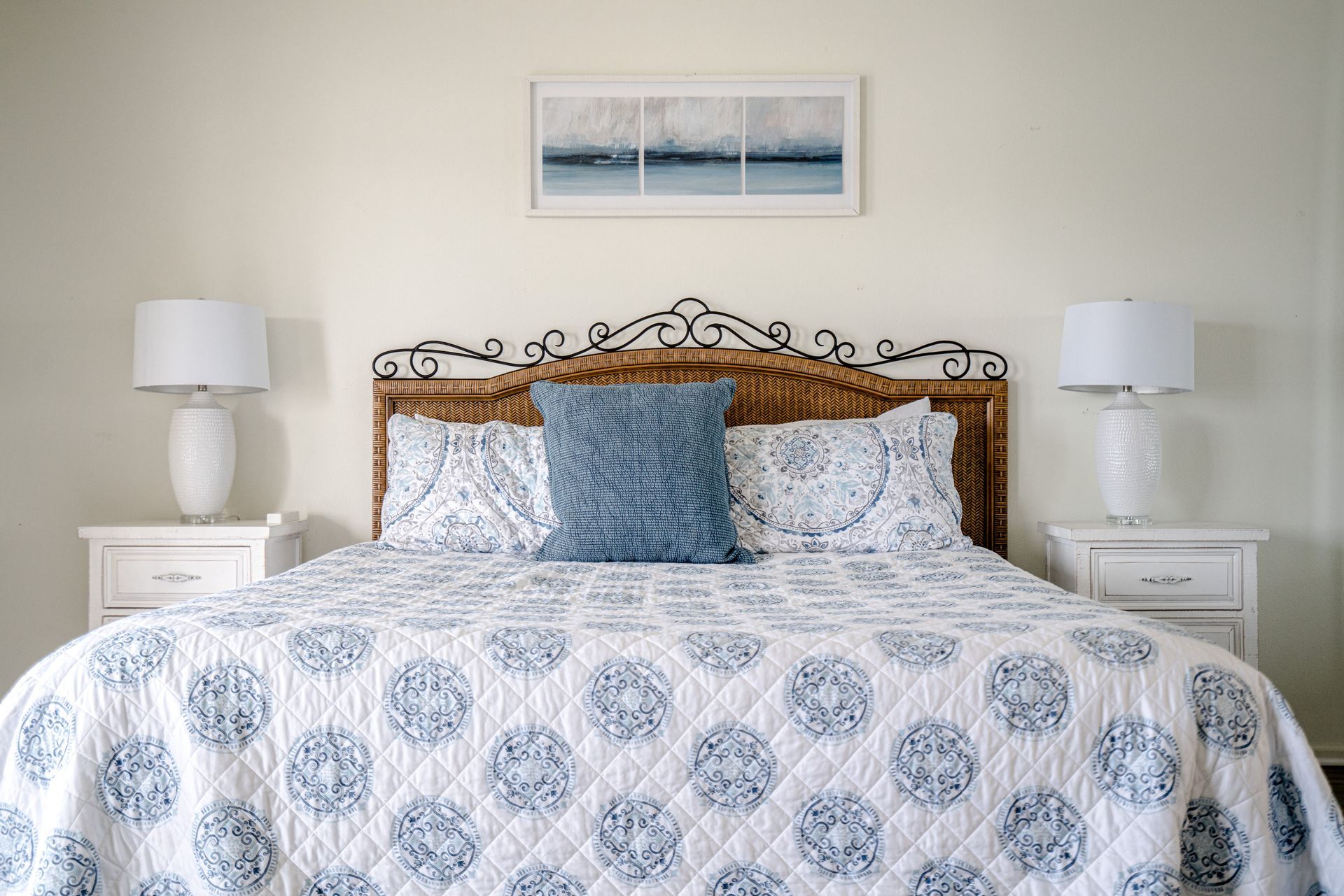A bedroom with a bed , nightstands , lamps and a picture on the wall above the bed.