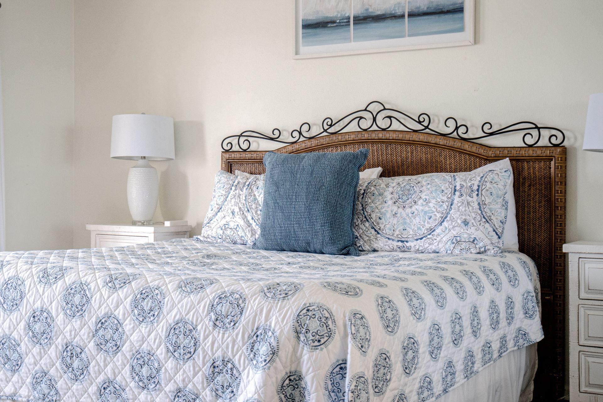 A bedroom with a bed , nightstand , lamp and picture on the wall.