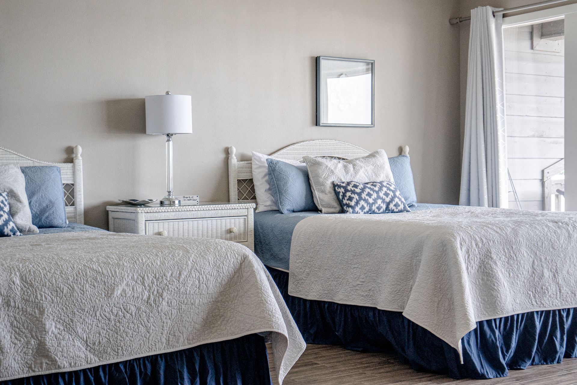 A bedroom with two beds , a nightstand , a lamp and a window.