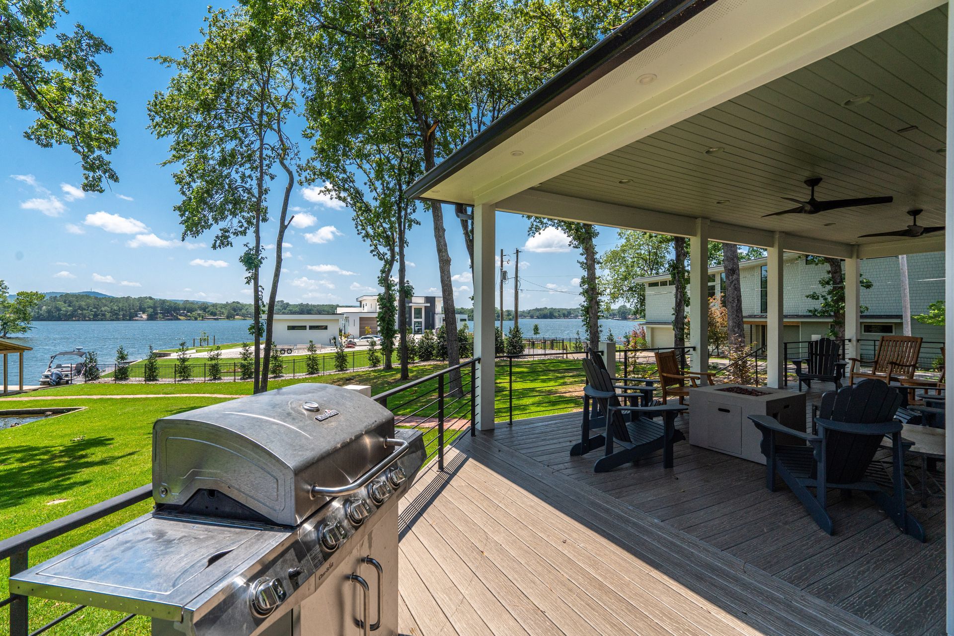 There is a grill on the deck of a house with a view of the lake.