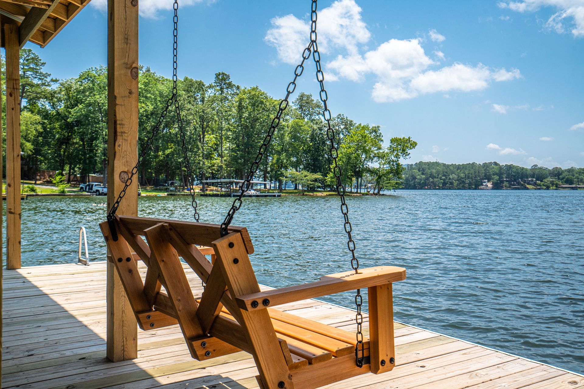 A wooden swing is hanging from a dock overlooking a lake.