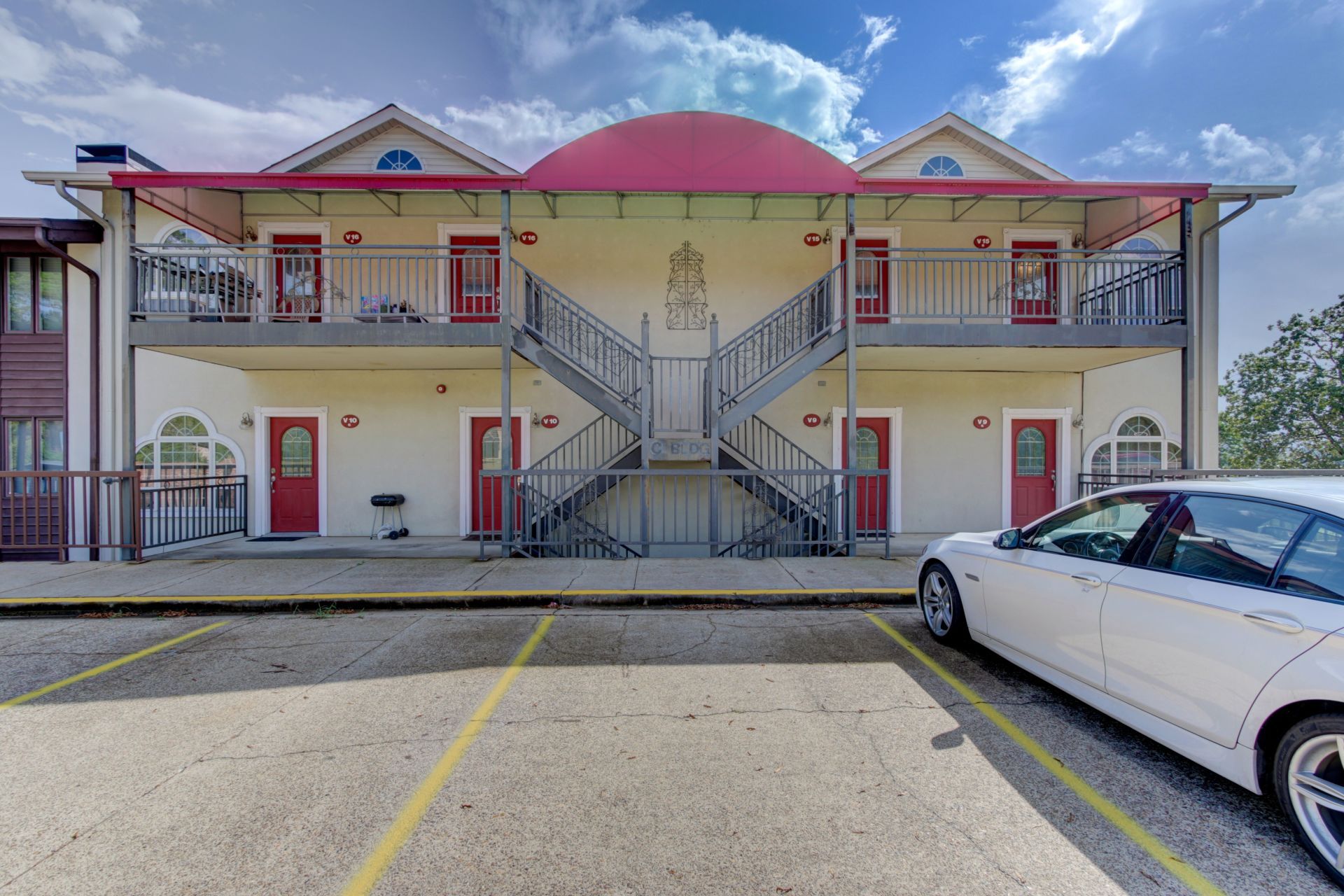A white car is parked in front of a large white building.