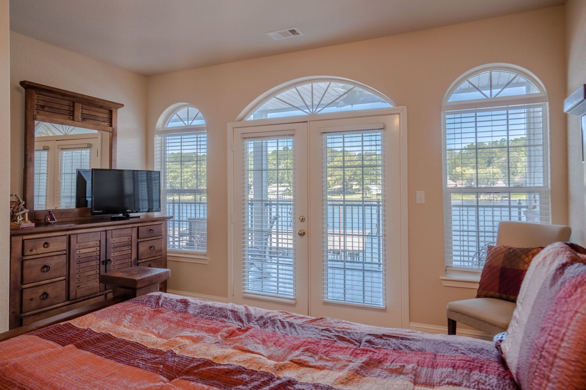 A bedroom with a king size bed , dresser , television and sliding glass doors.