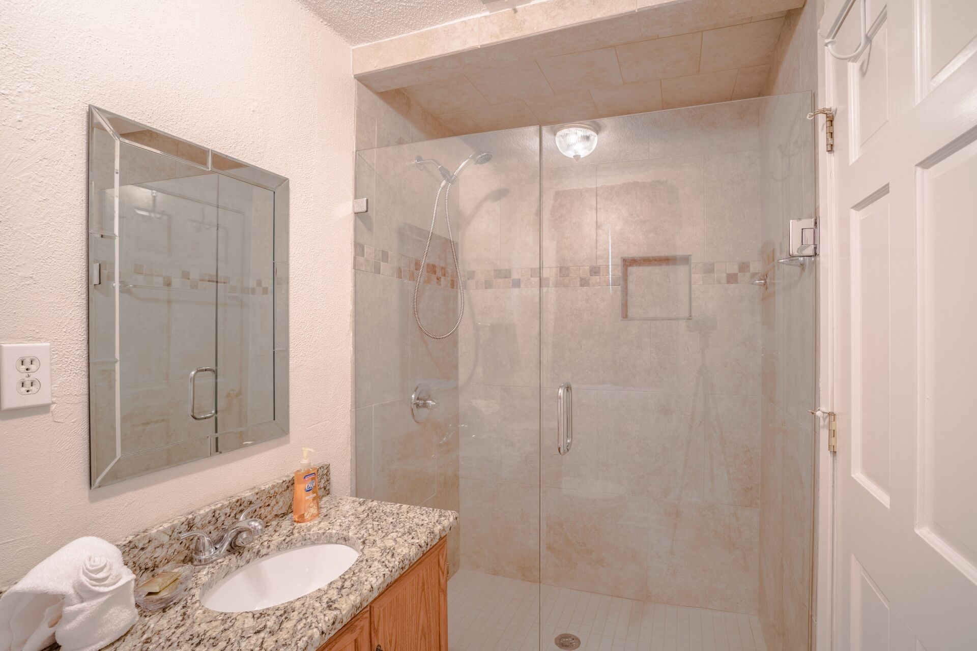 A bathroom with a sink , mirror and walk in shower.