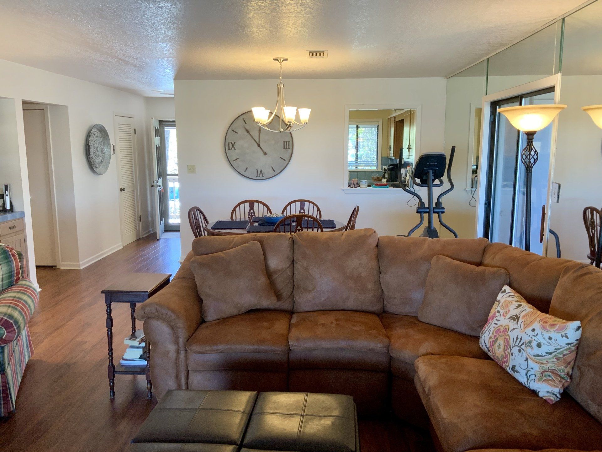 A living room with a brown sectional couch and a clock on the wall
