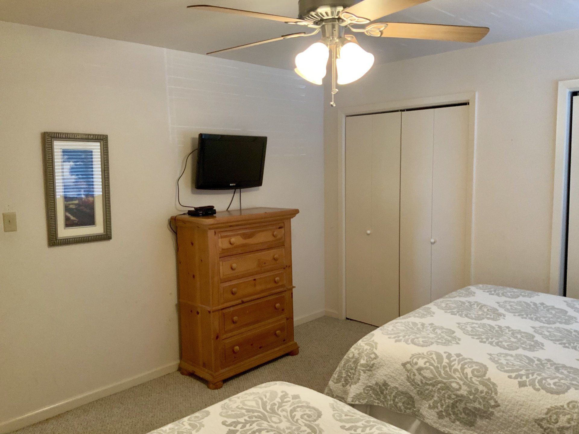 A bedroom with two beds , a dresser , a television and a ceiling fan.