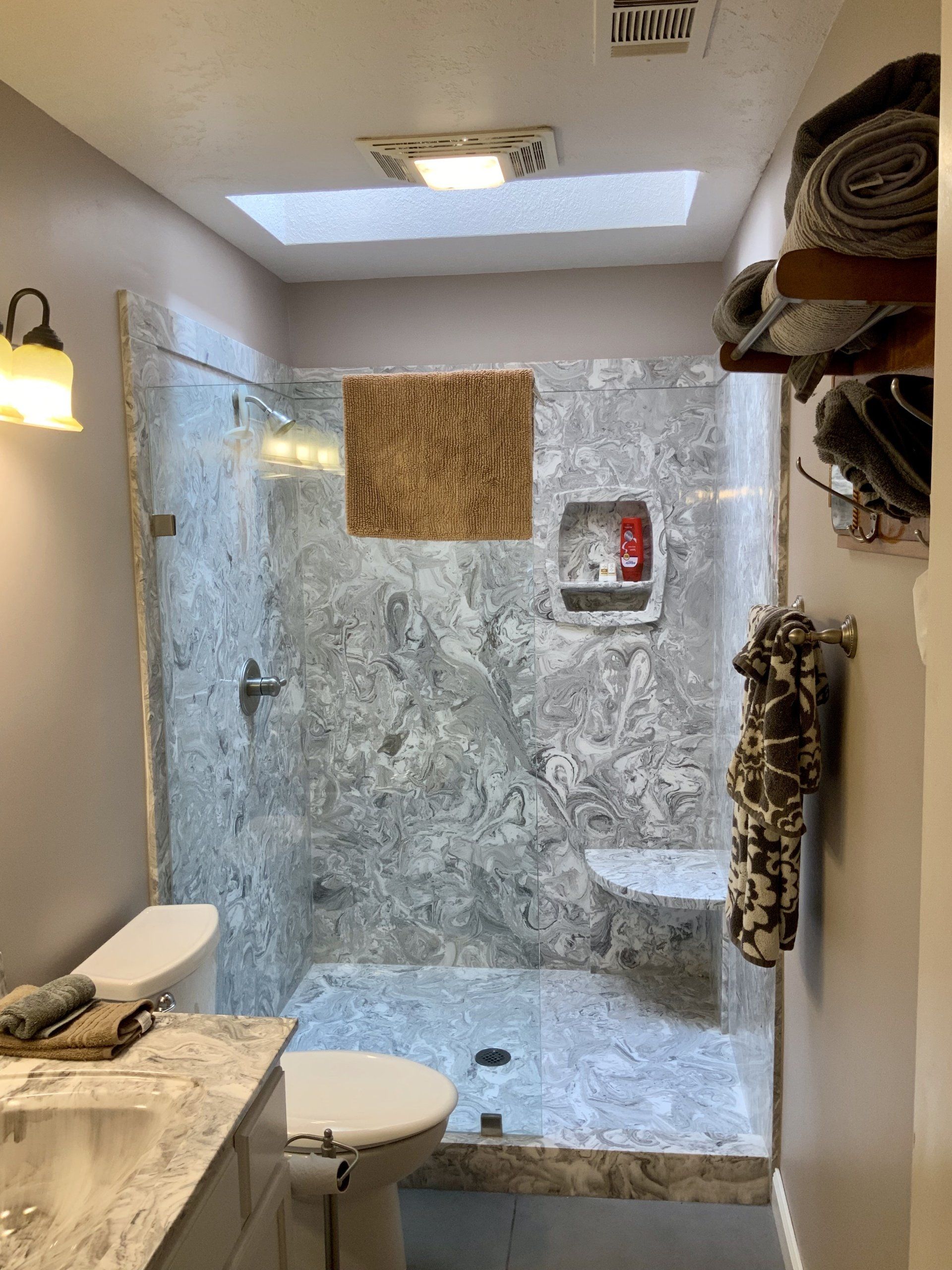 A bathroom with a toilet , sink , shower and skylight.