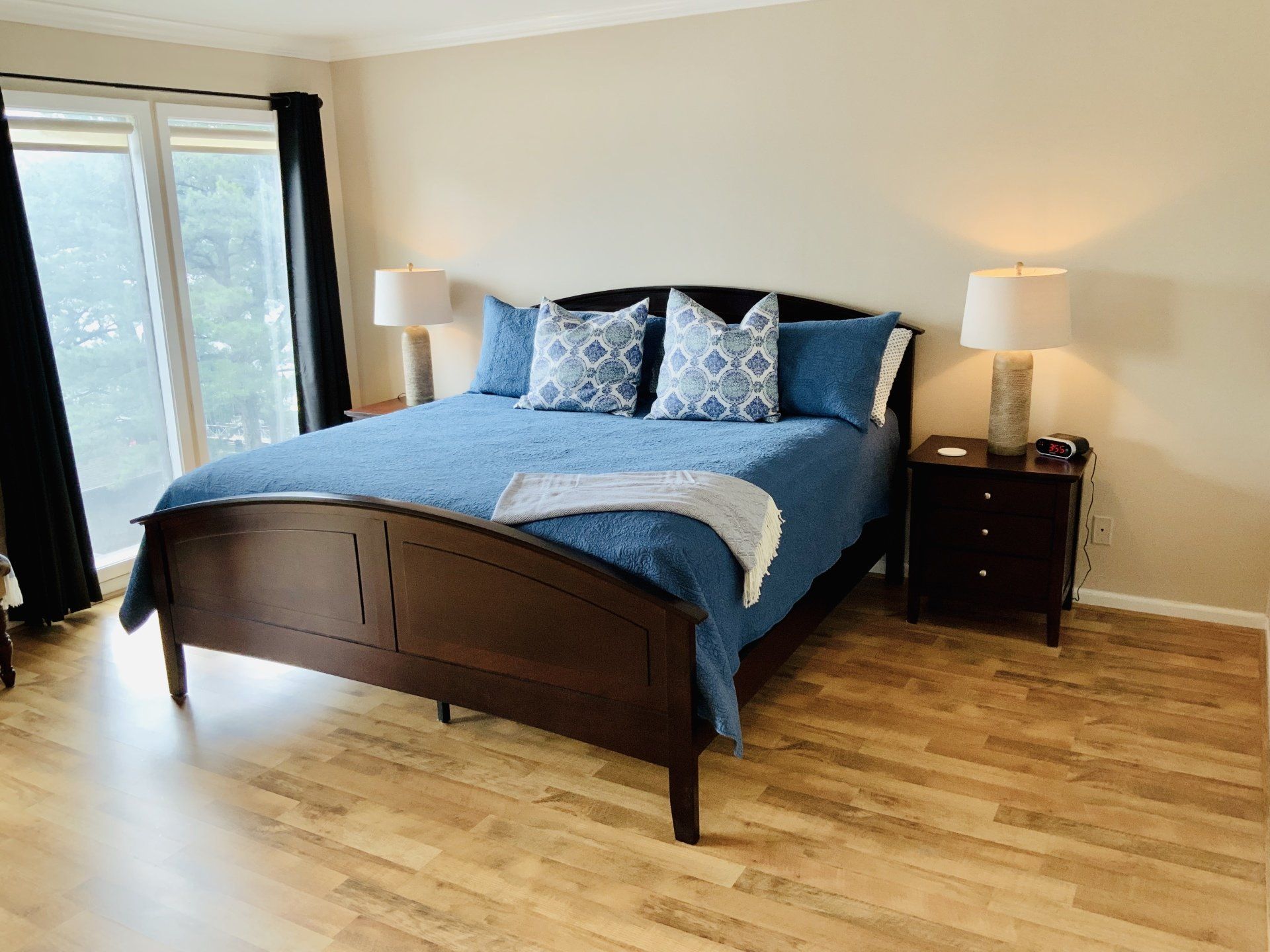 A bedroom with a king size bed , nightstand , lamps and a large window.