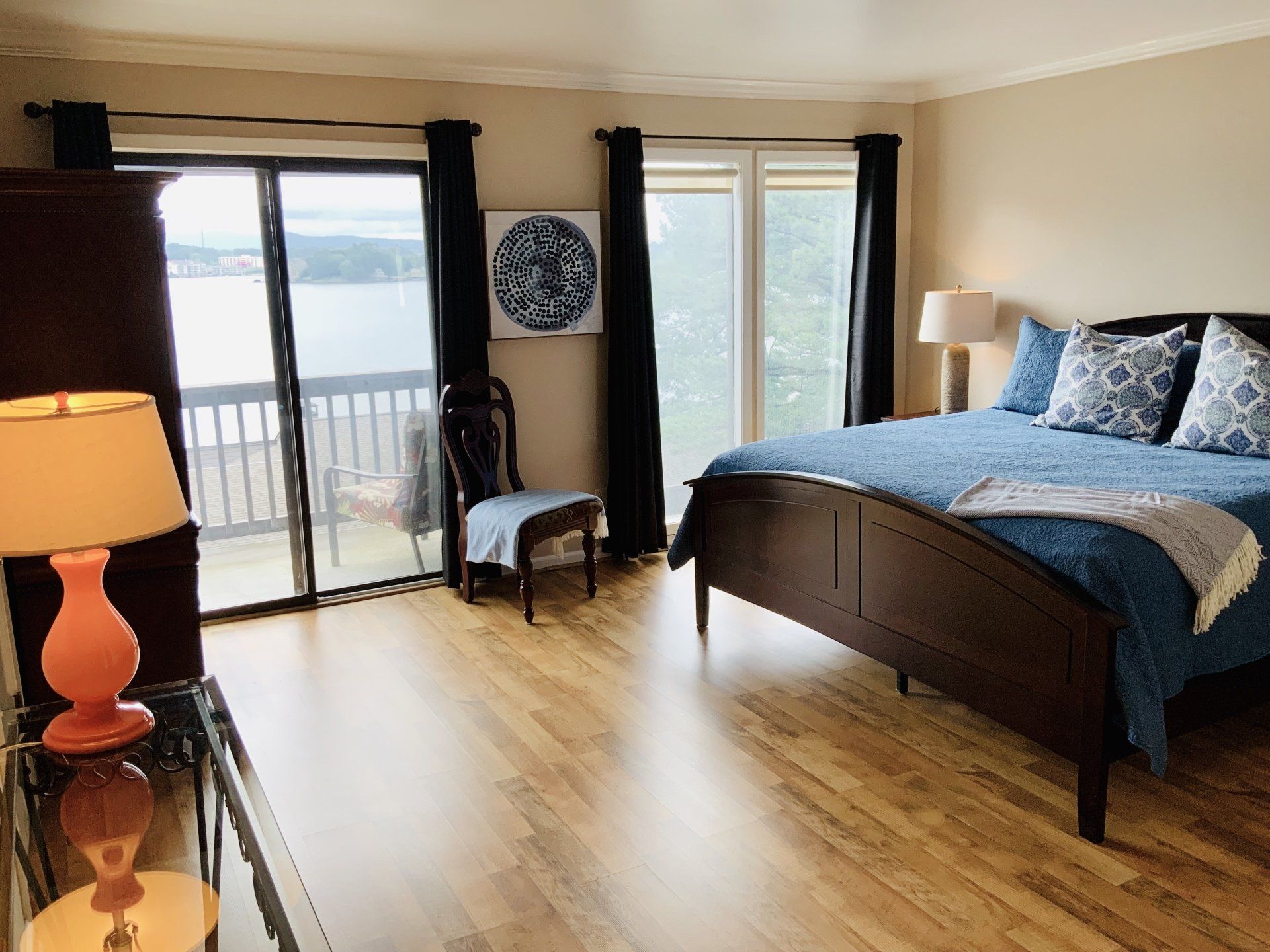 A bedroom with a king size bed , chair , lamps and sliding glass doors.