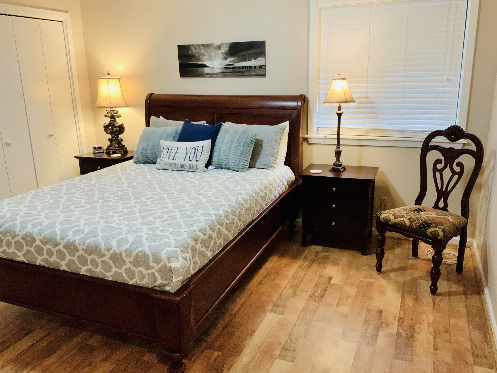 A bedroom with a bed , nightstand , chair and lamps.