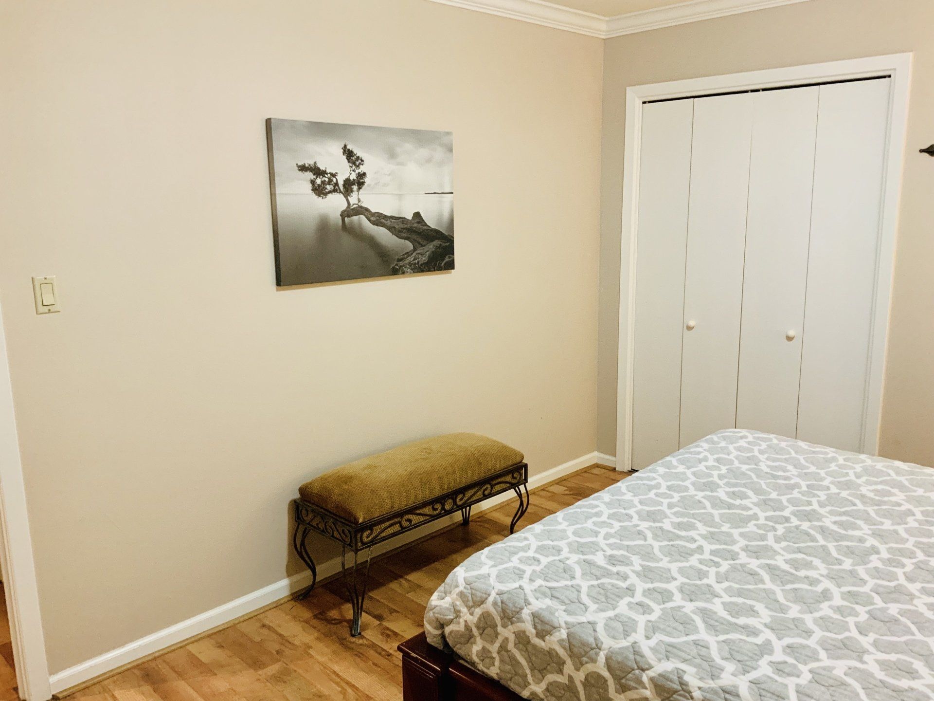 A bedroom with a bed , bench and a painting on the wall.