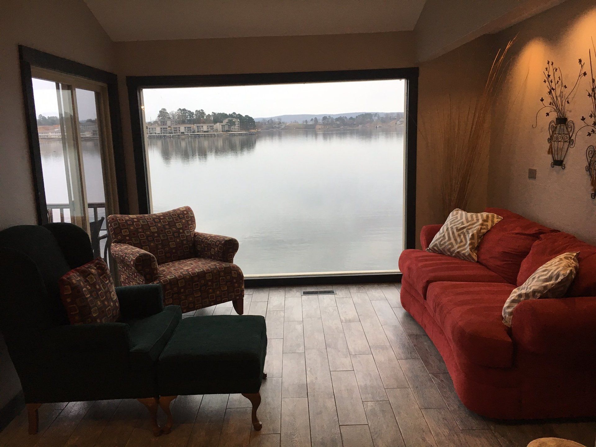 A living room with a couch , chair , ottoman and large window overlooking a lake.