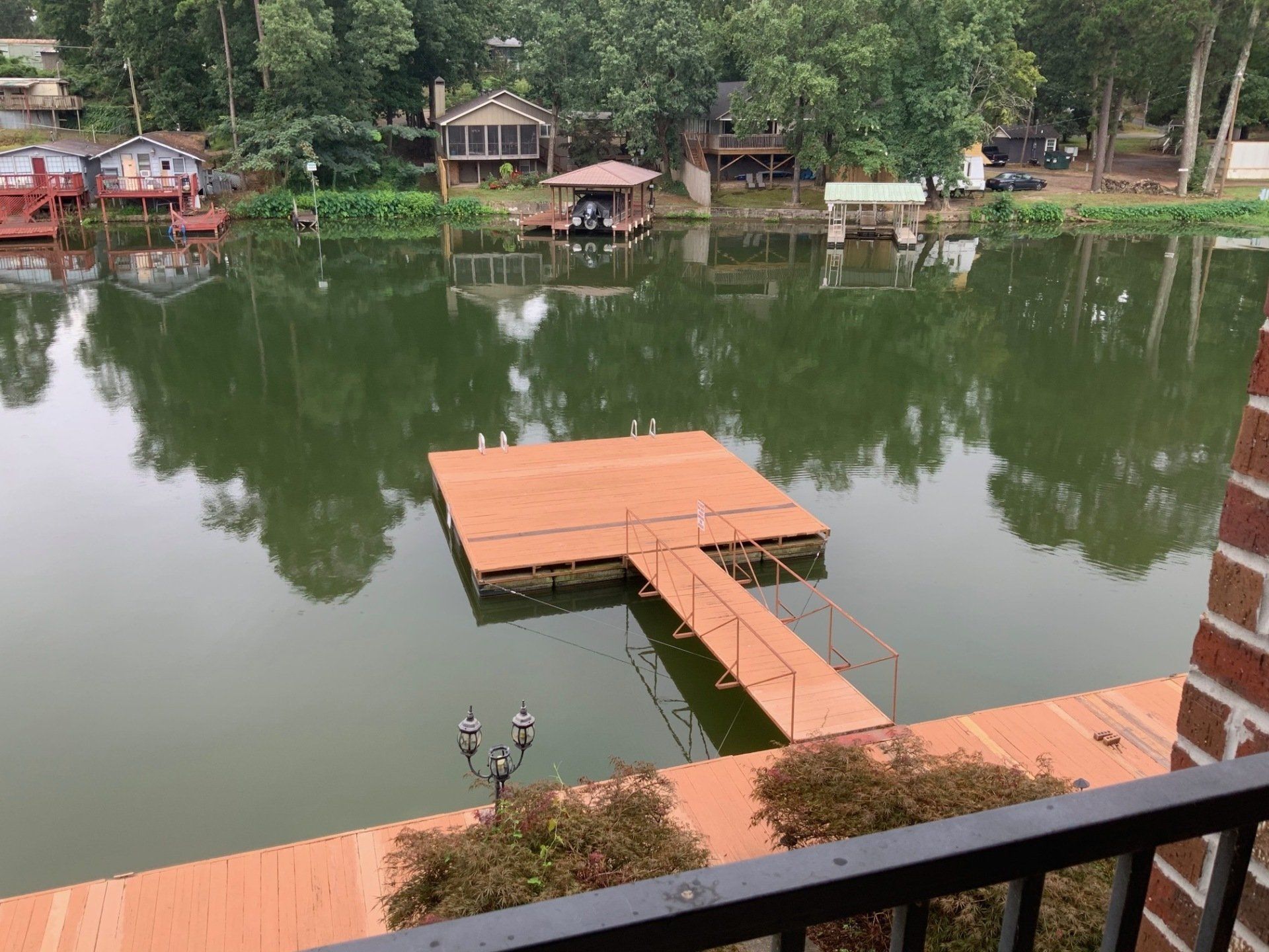 A view of a lake from a balcony with a dock in the middle of it.