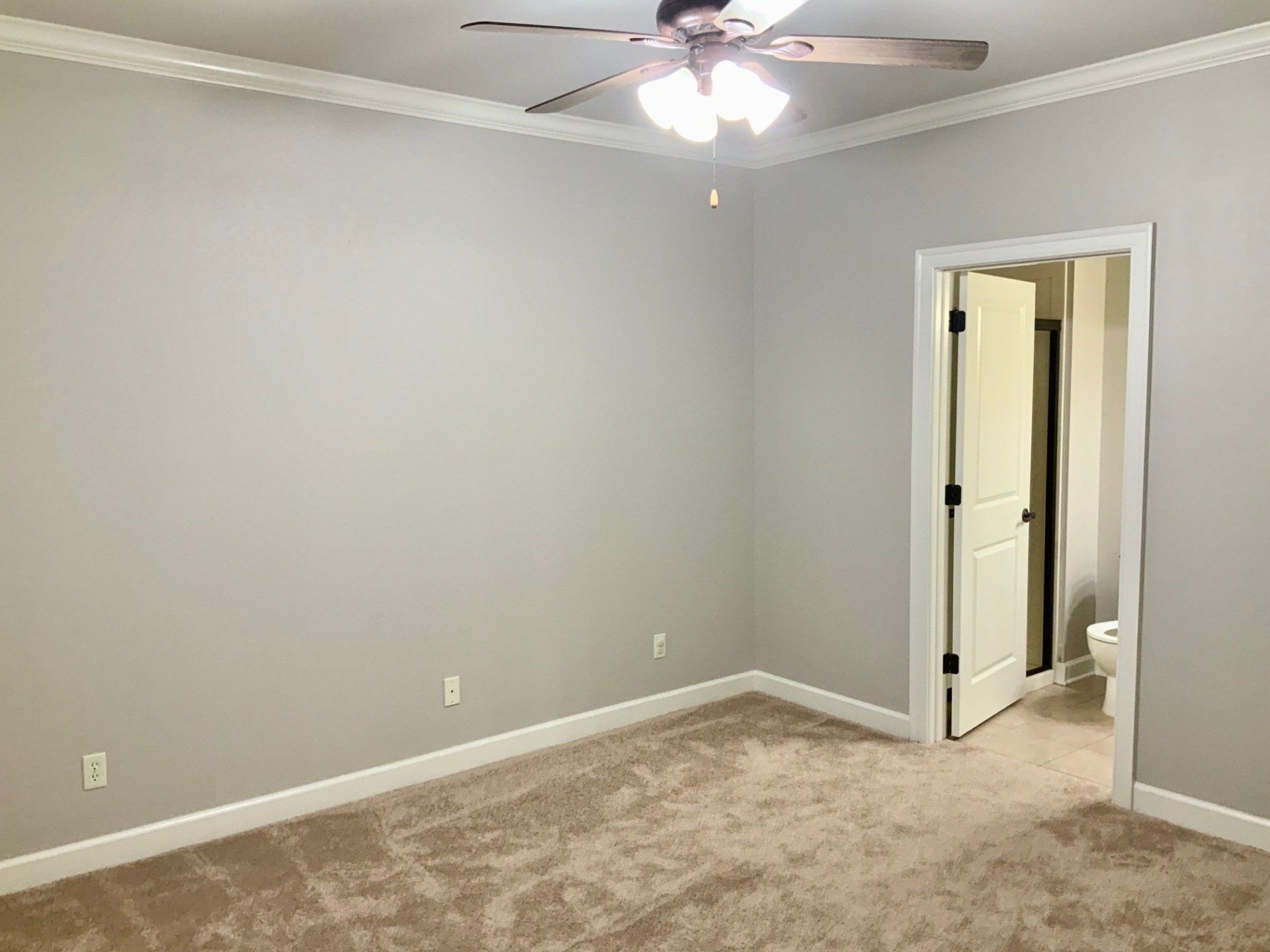 An empty bedroom with a ceiling fan and a toilet.