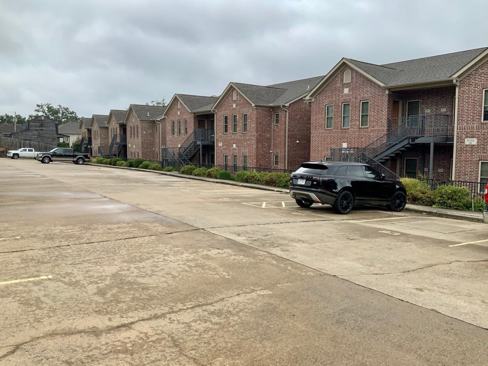 A black car is parked in front of a row of apartment buildings.
