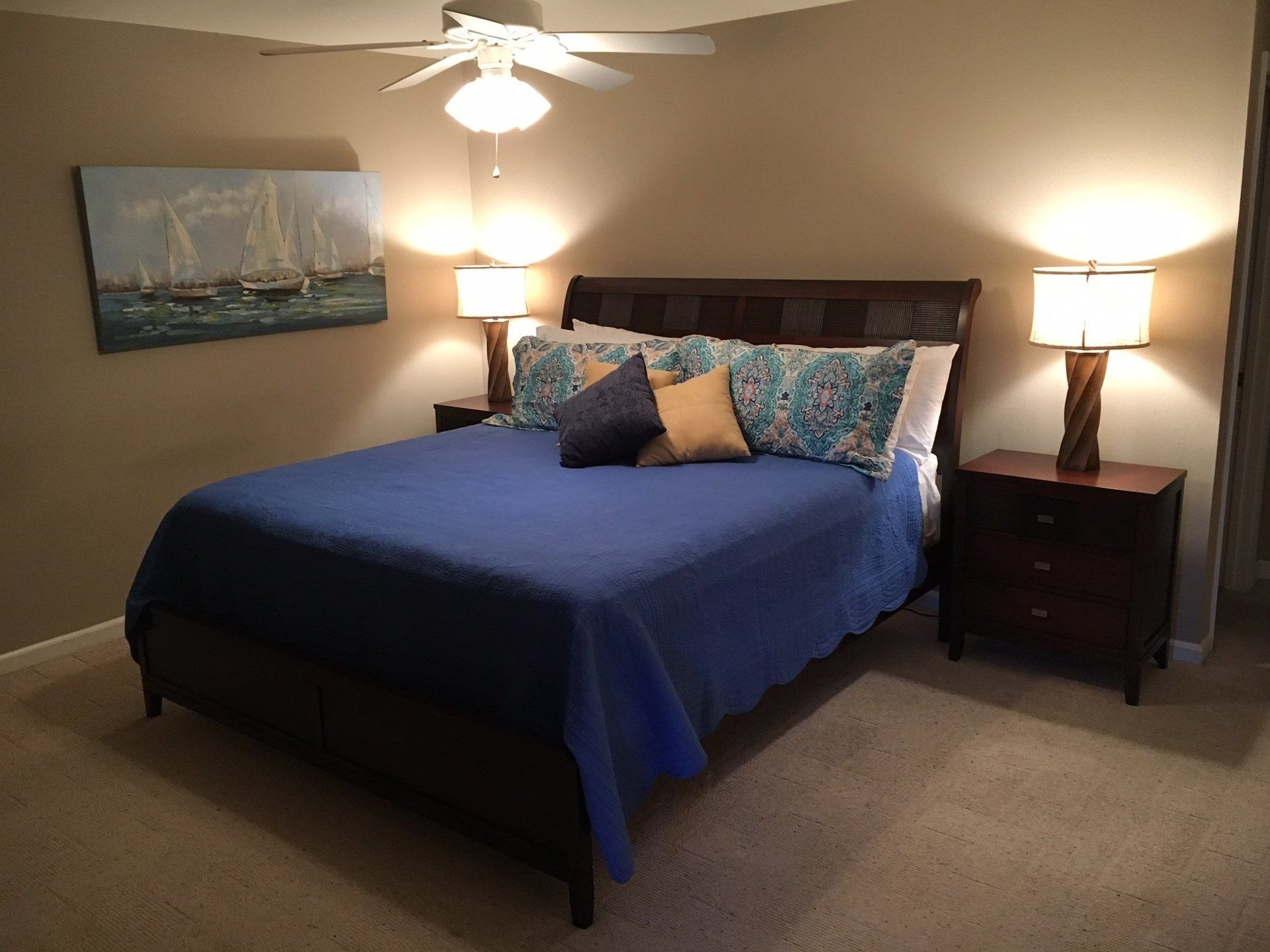 A bedroom with a king size bed , nightstands , lamps and a ceiling fan.