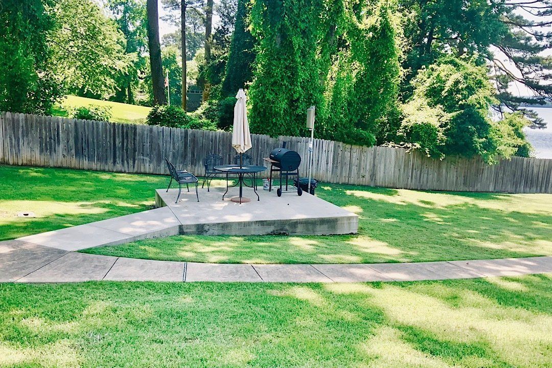 A patio area with a table and chairs in the middle of a lush green yard.