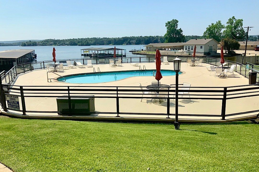 A large swimming pool surrounded by chairs and umbrellas next to a lake.