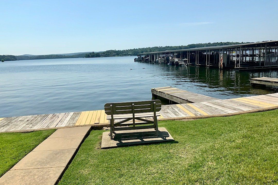 A bench is sitting on the grass next to a dock overlooking a lake.