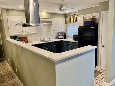 A kitchen with white cabinets , a black refrigerator , and a stainless steel hood.