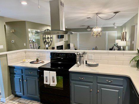 A kitchen with blue cabinets , a black stove , and white counter tops.