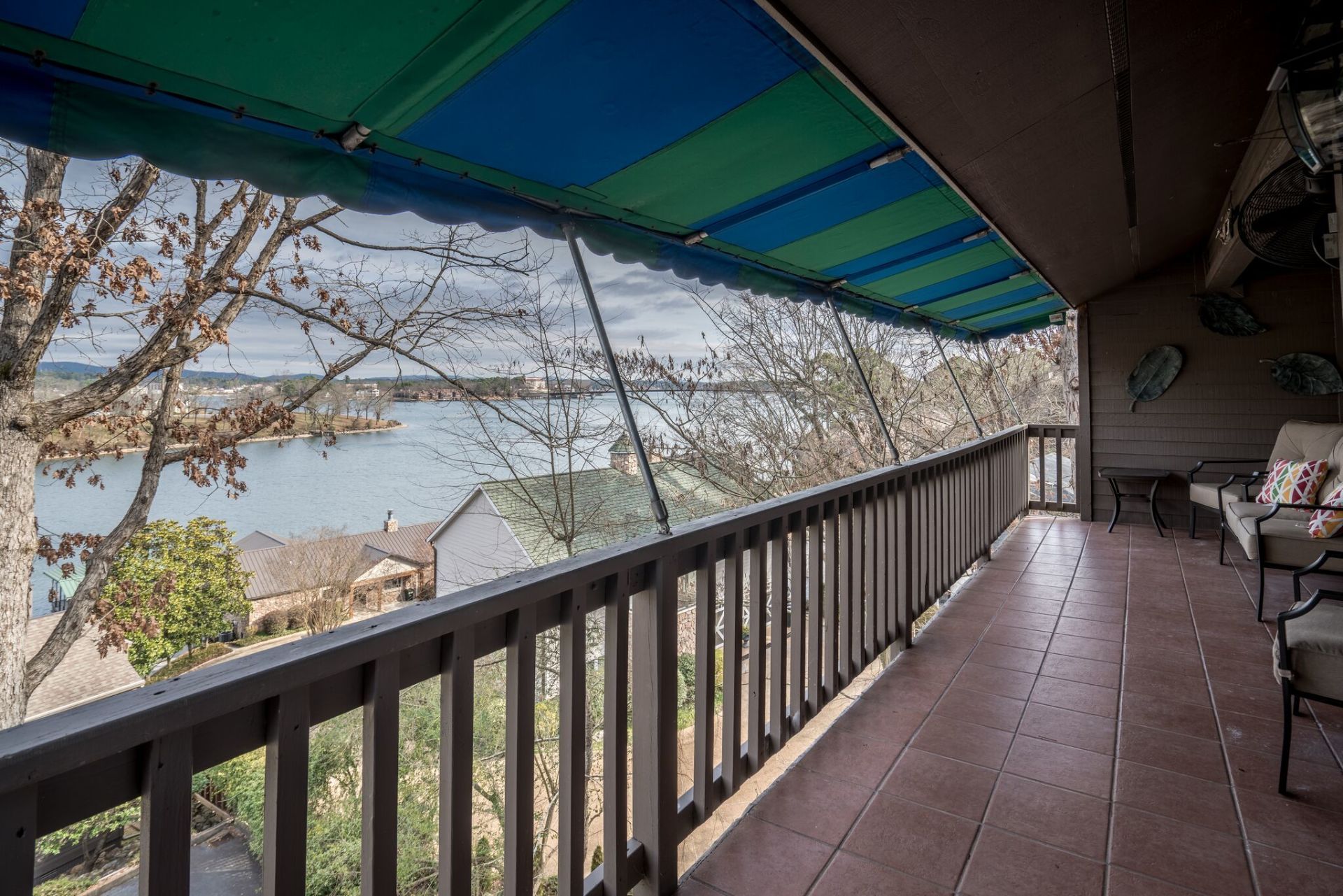 A balcony with a blue and green awning overlooking a lake.