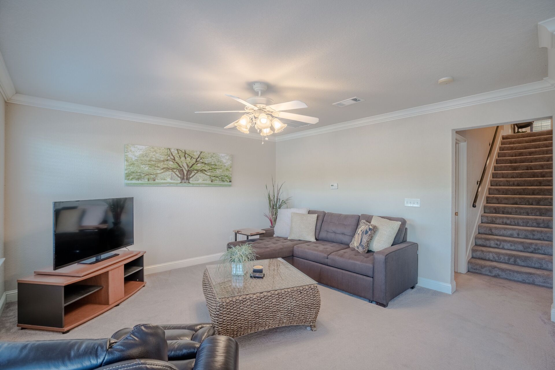 A living room with a couch , television , coffee table and stairs.
