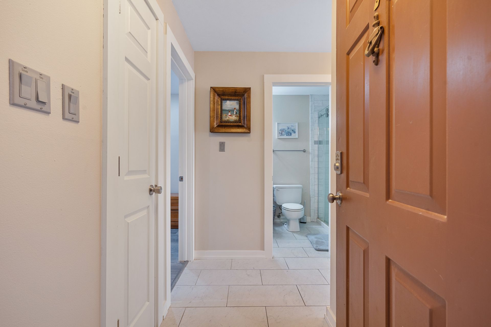 A hallway with a door open leading to a bathroom and a toilet.