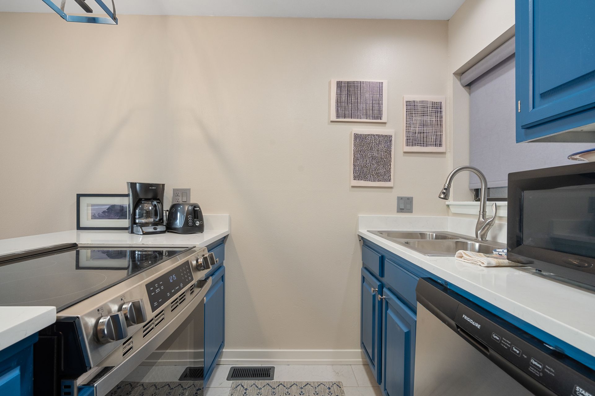 A kitchen with blue cabinets , a stove , a microwave , and a sink.