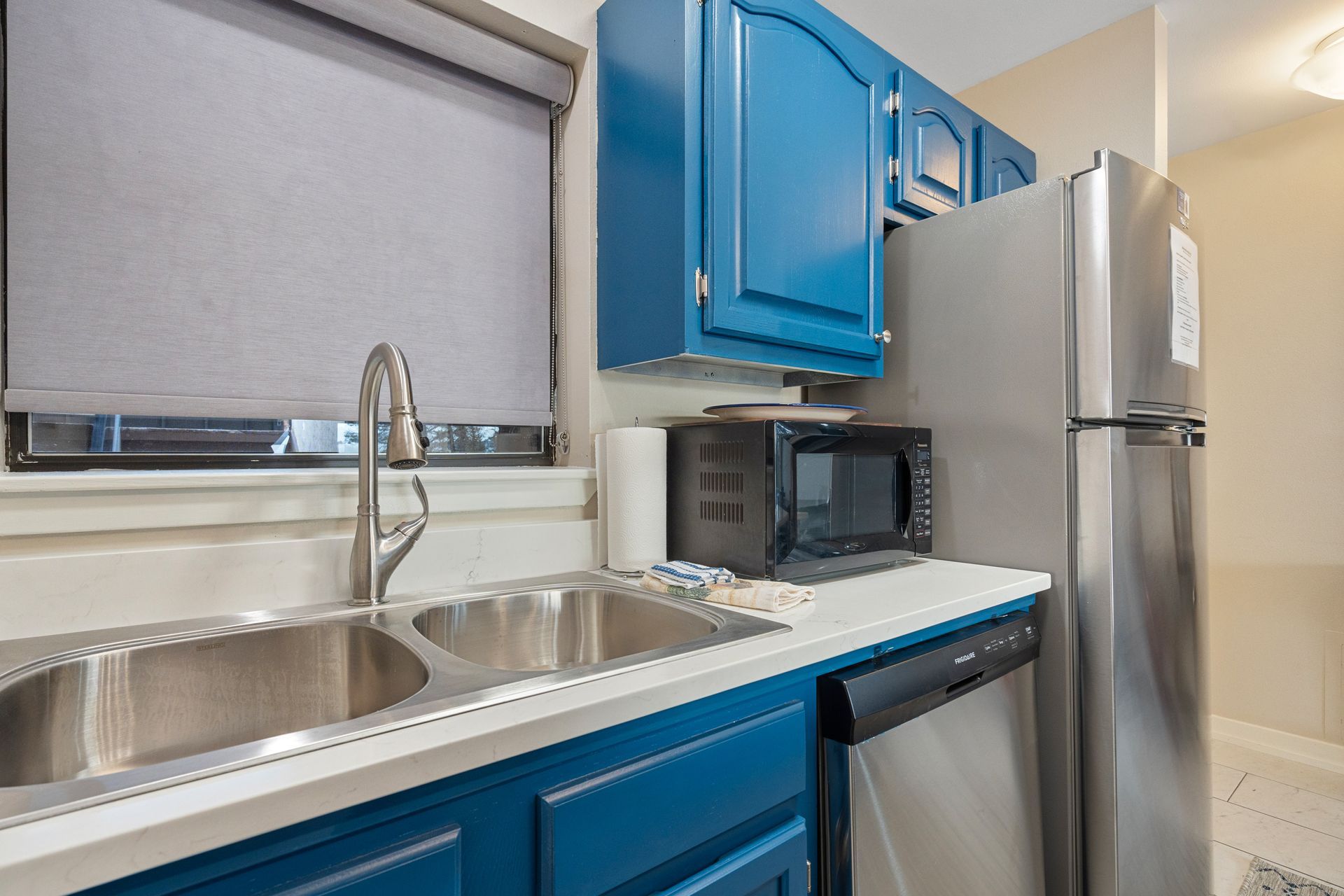 A kitchen with blue cabinets , stainless steel appliances , a sink and a refrigerator.