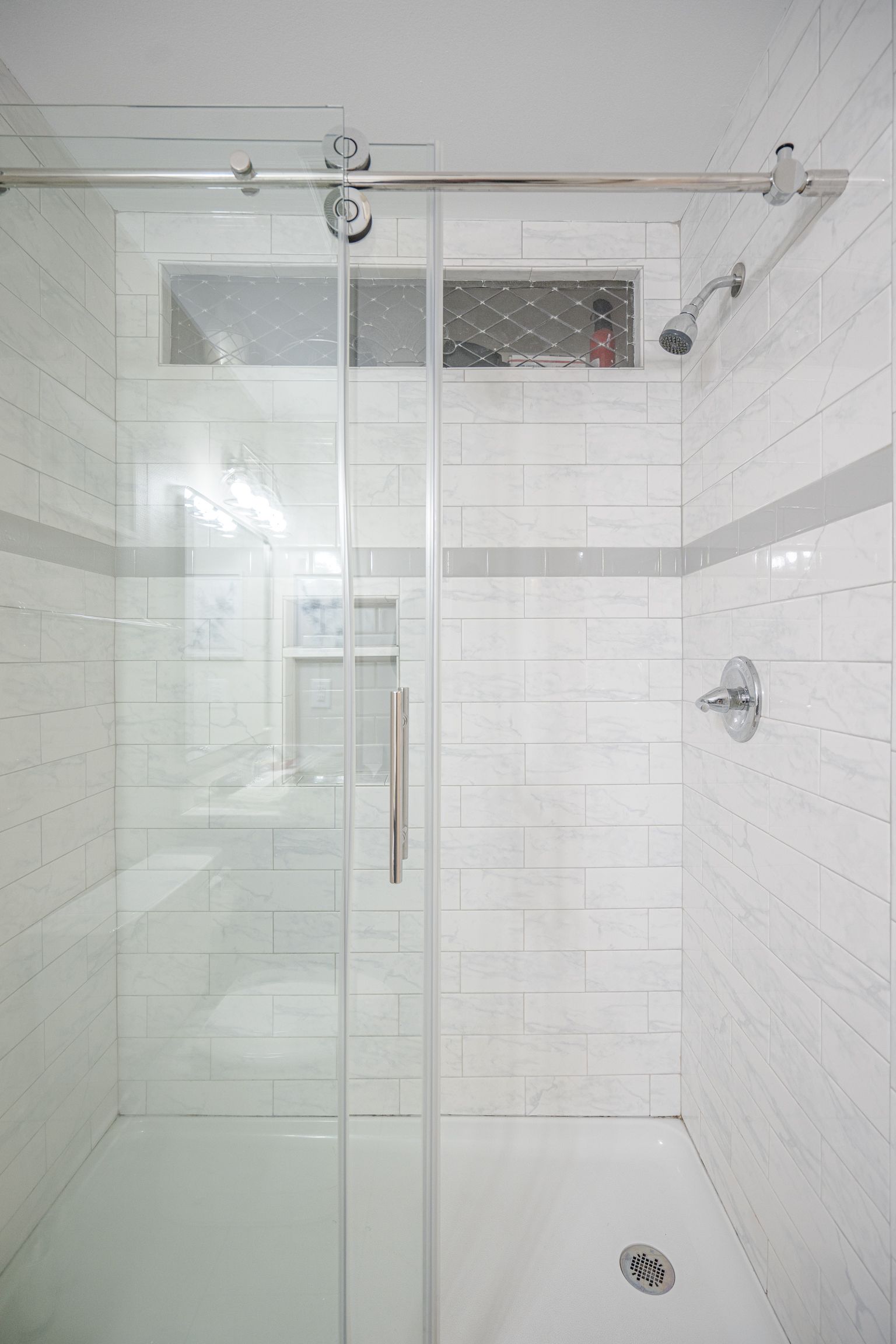 A bathroom with white tiles and a sliding glass shower door.
