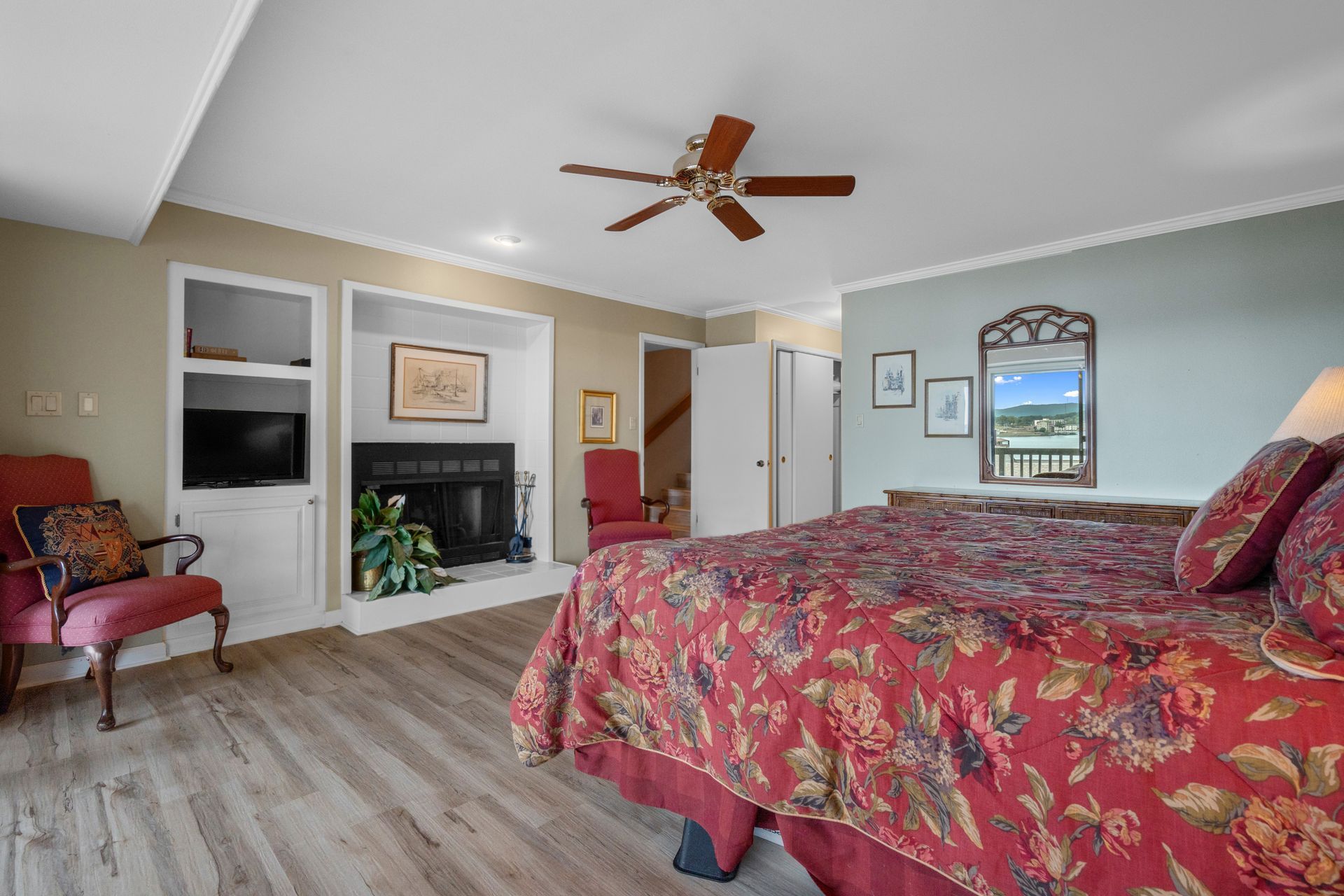 A bedroom with a bed , chair , fireplace and ceiling fan.
