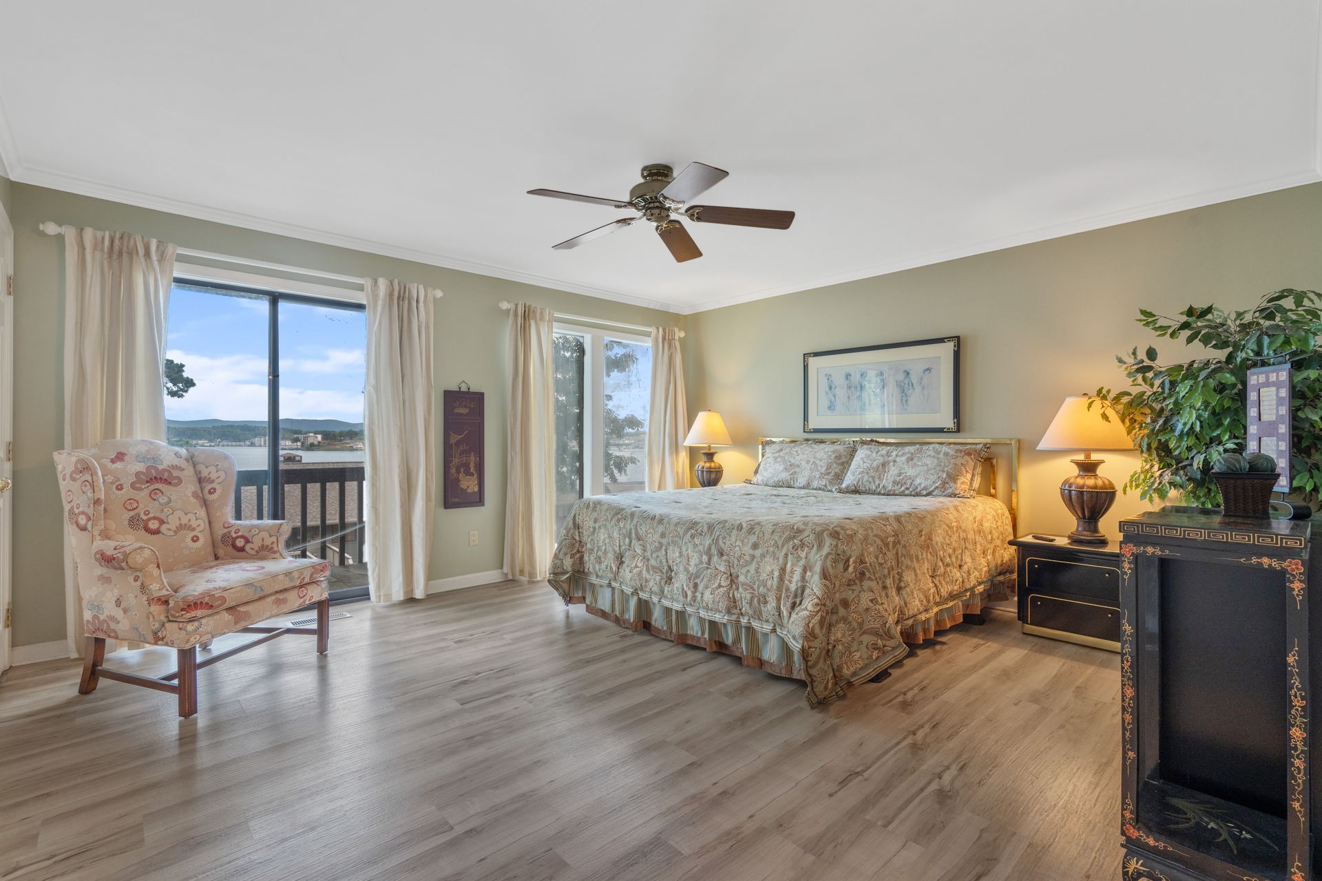 A large bedroom with a king size bed , chair , lamps and a ceiling fan.