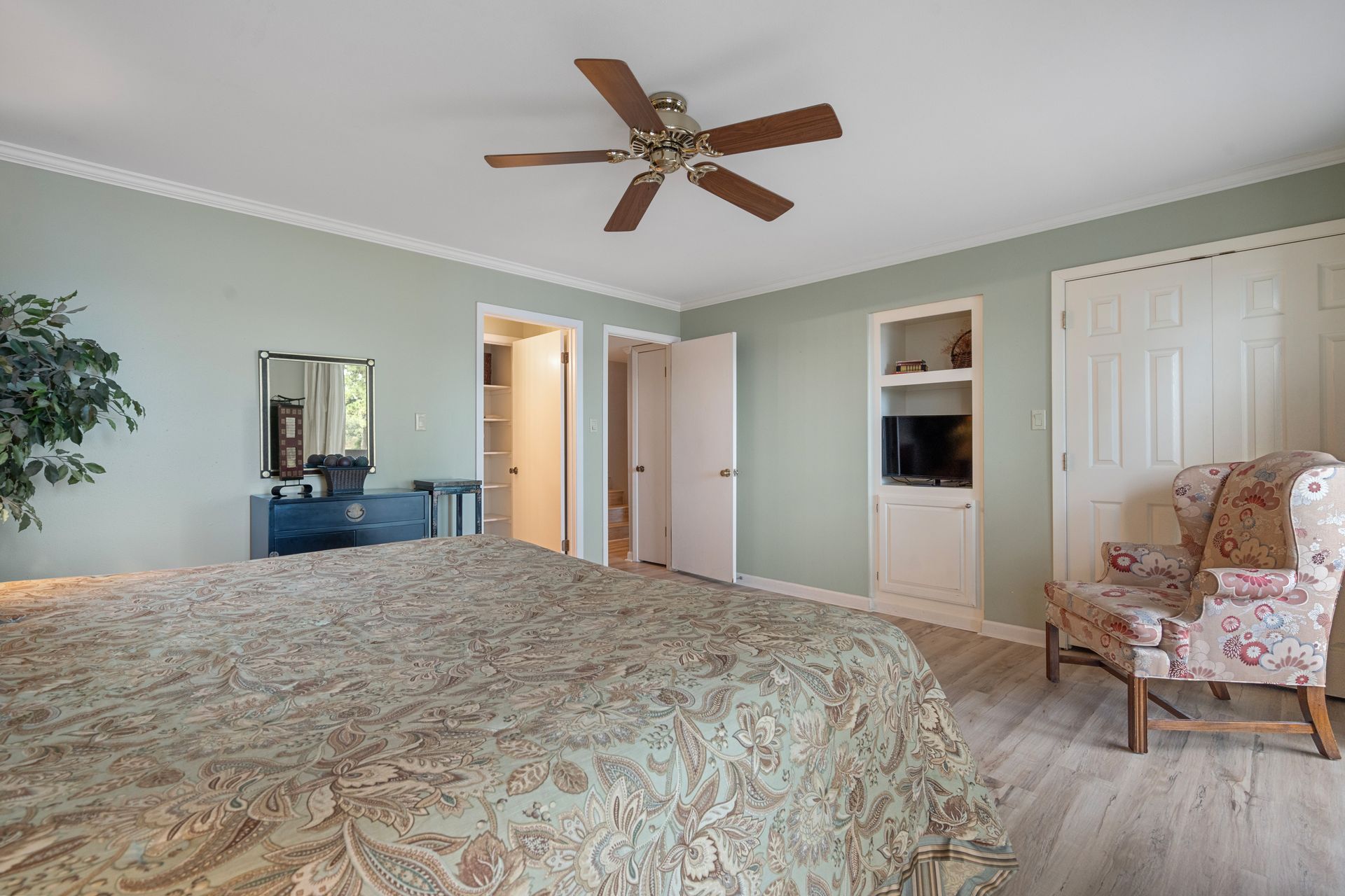 A bedroom with a bed , chair , dresser and ceiling fan.