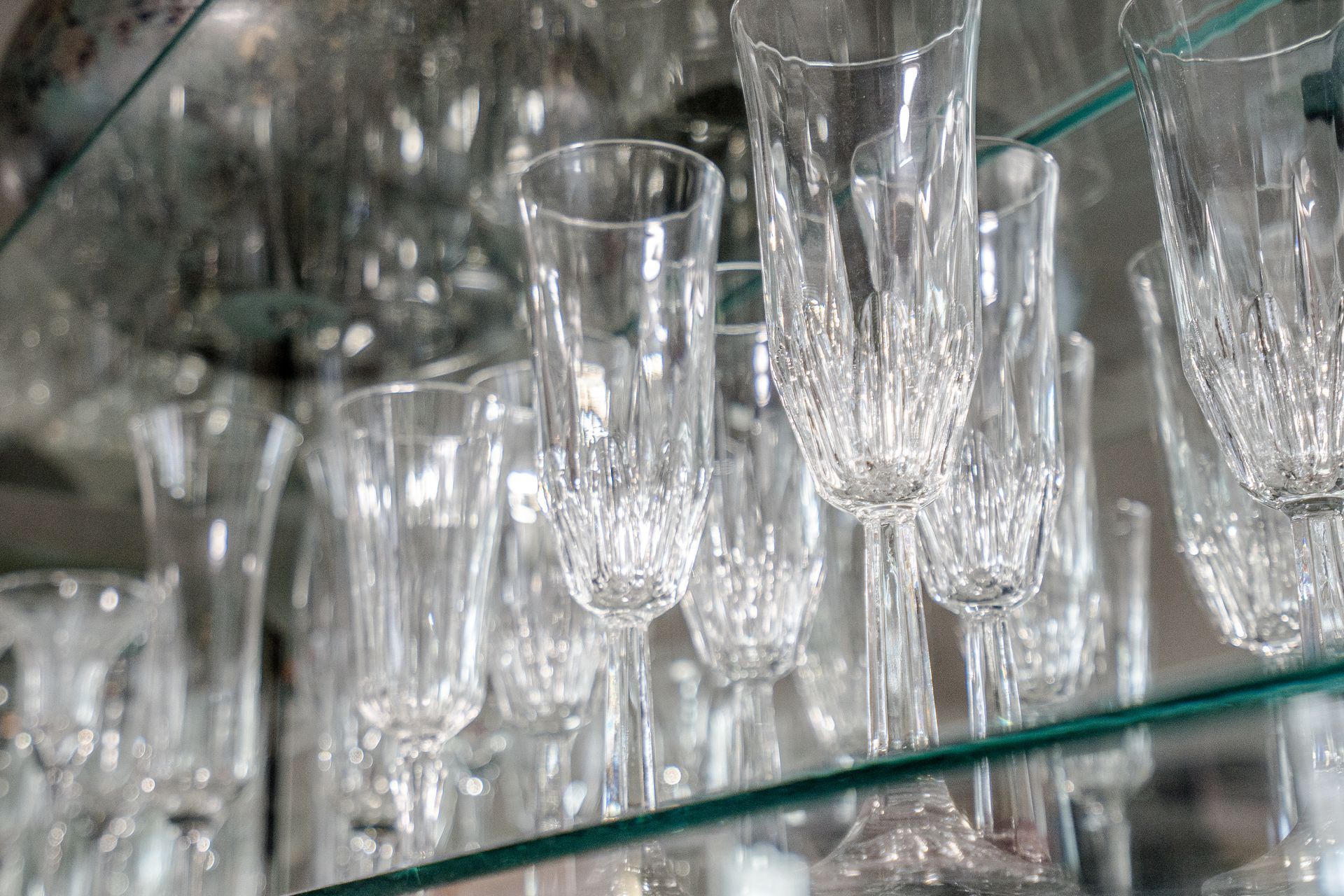 A row of wine glasses hanging on a glass shelf.