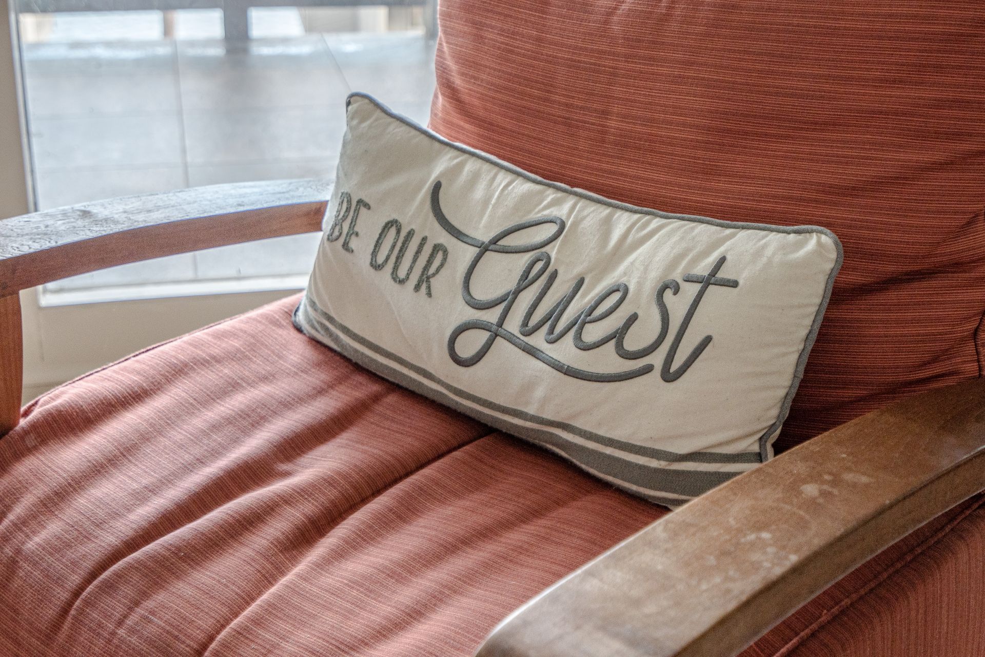 A pillow that says `` be our guest '' is sitting on a chair.