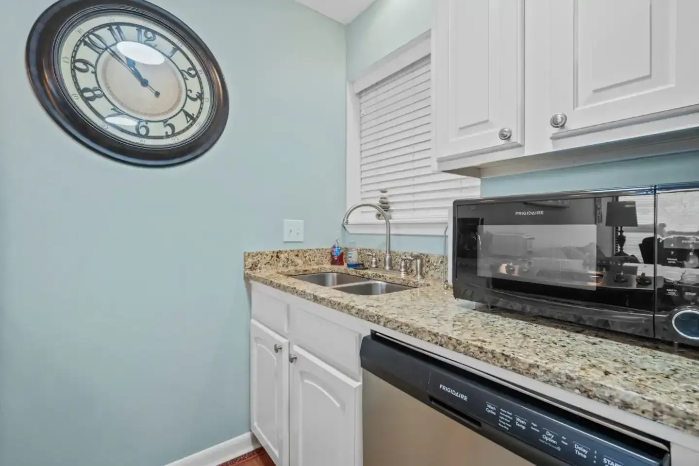 A kitchen with a sink , dishwasher , microwave and clock on the wall.