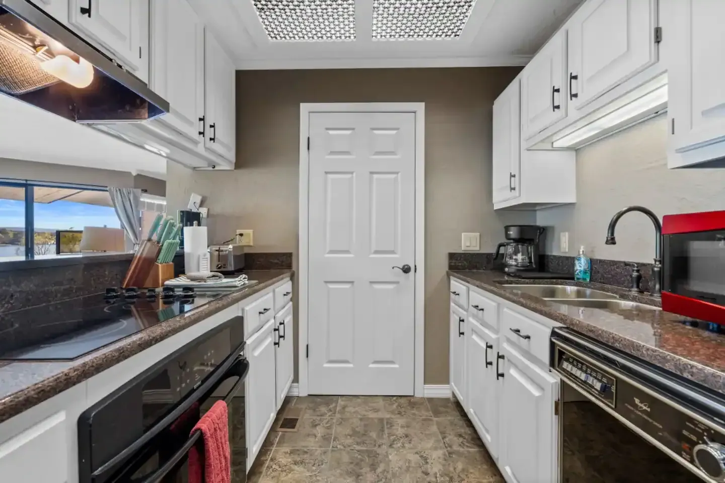 A kitchen with white cabinets , a stove , a sink , and a microwave.
