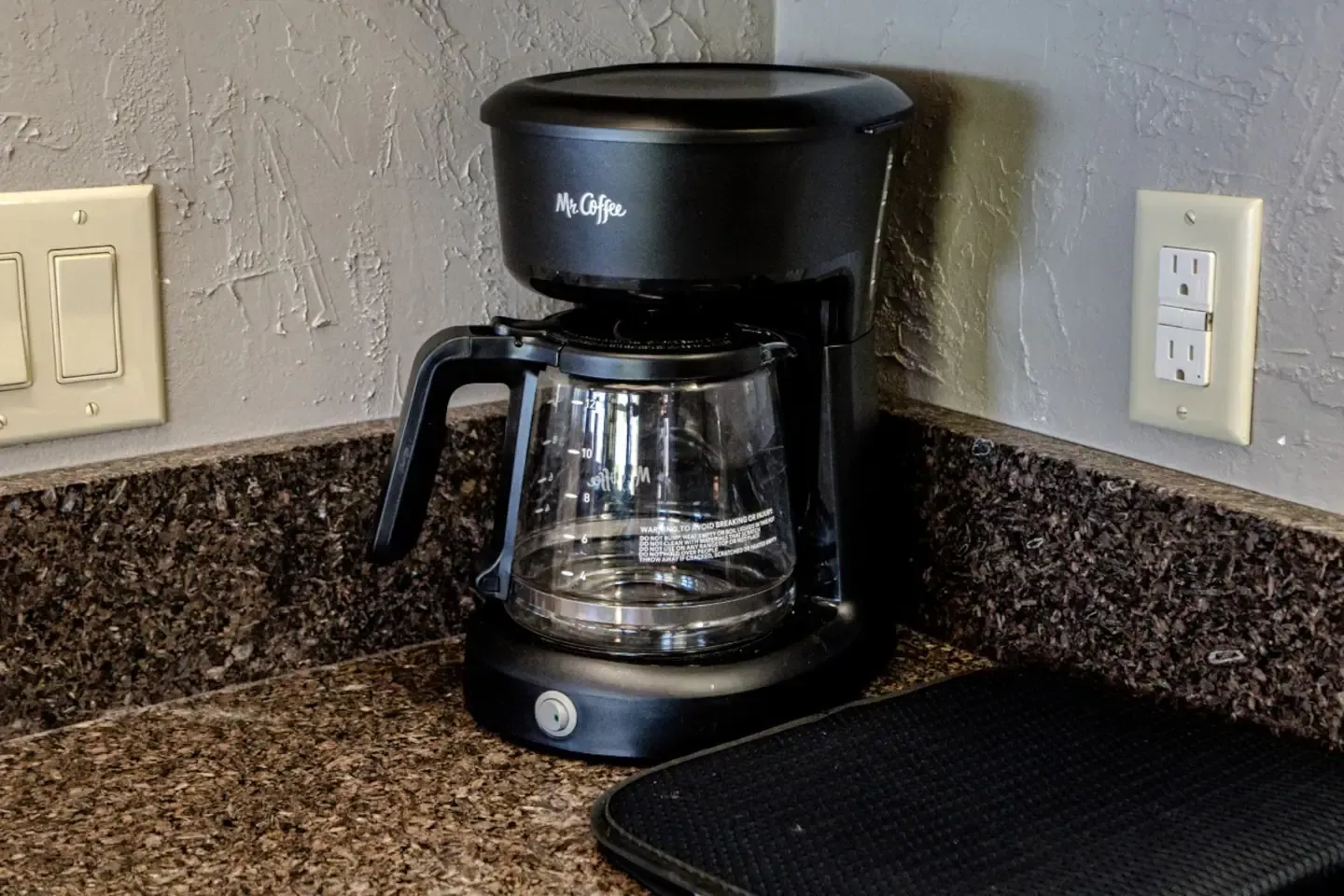 A black coffee maker is sitting on a granite counter.