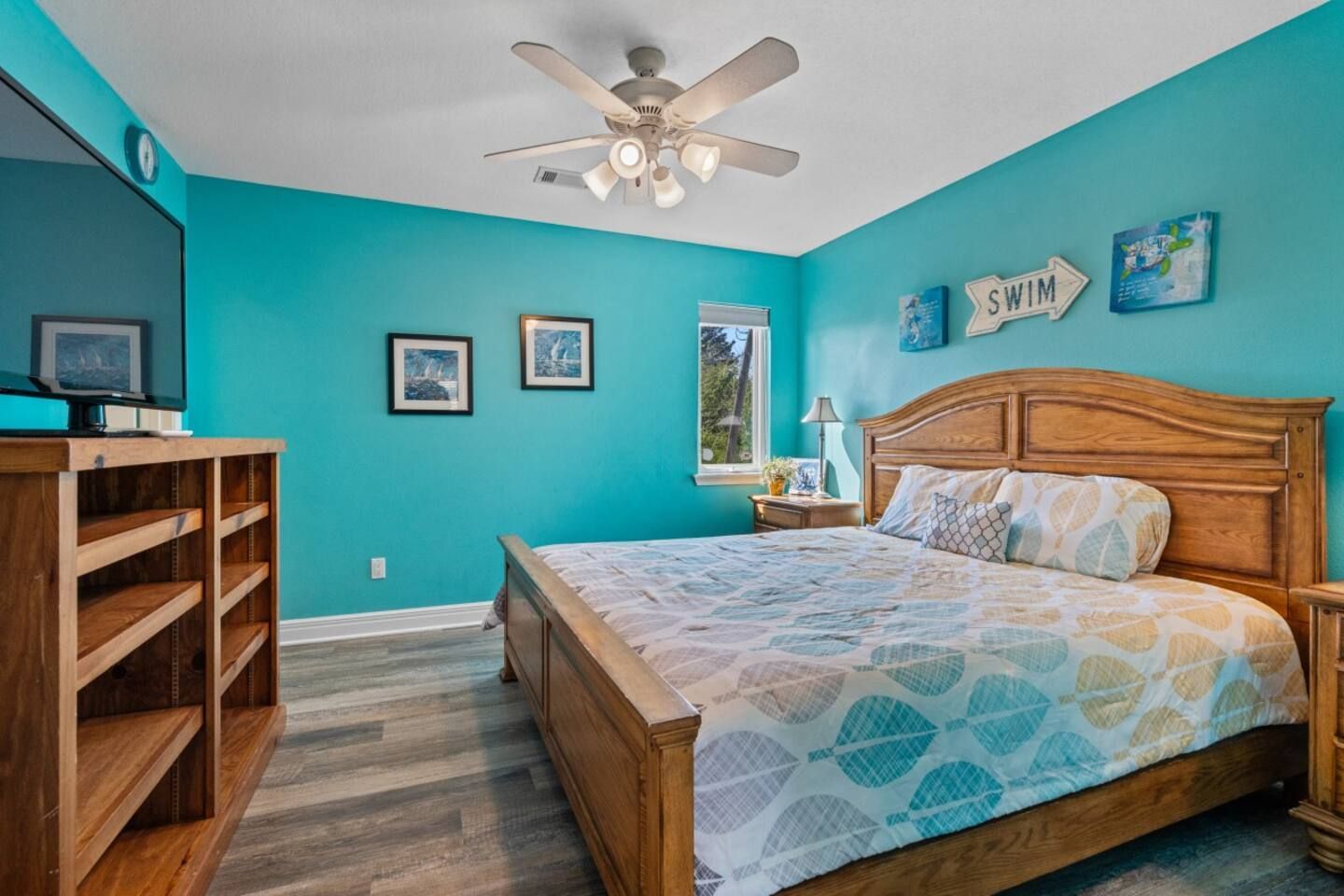 A bedroom with blue walls , a king size bed , a television and a ceiling fan.