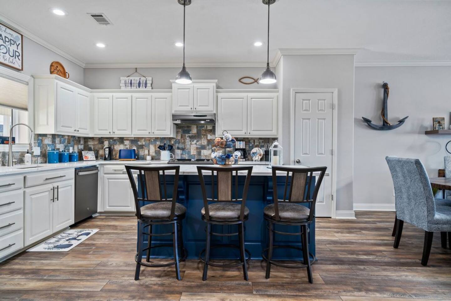 A kitchen with white cabinets and a blue island with three chairs.