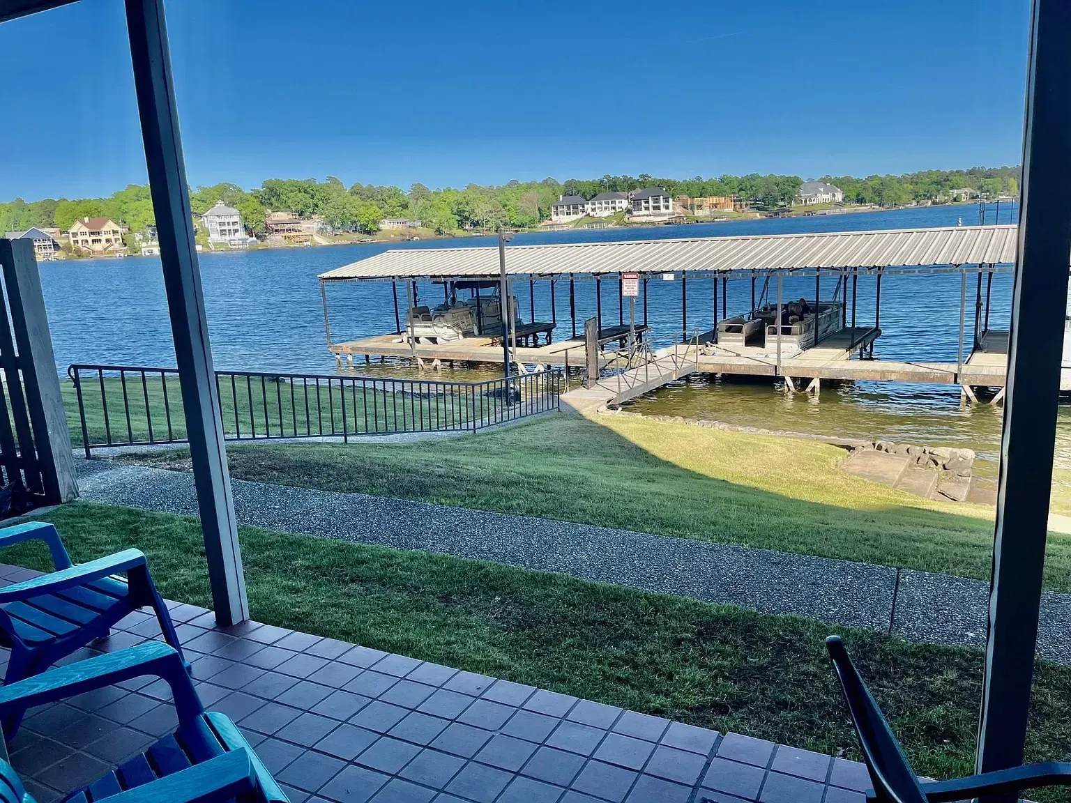 A view of a lake from a porch with chairs and a dock.